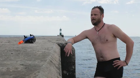Swimmer with a beard is standing on a concrete pier after swimming in the sea Stock Footage 109800291