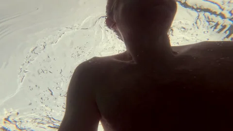 Swimmer with goggles looking up at the vibrant pink and orange sunset reflection Stock Footage 339810015