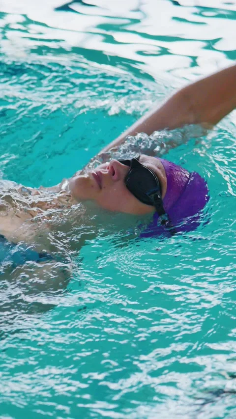 Swimmer with purple cap and goggles strokes through clear water Stock Footage 346458876