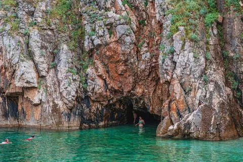 Swimmers explore a hidden cave in a tranquil turquoise water lagoon Stock Photos