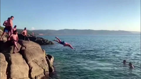 Swimming and jumping over the rocks on the beach of Marsa El-Zaitoun Stock Footage