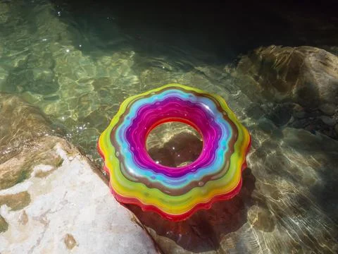 Swimming circle with multicolored patterns in a clear river with a rocky bottom 스톡 사진