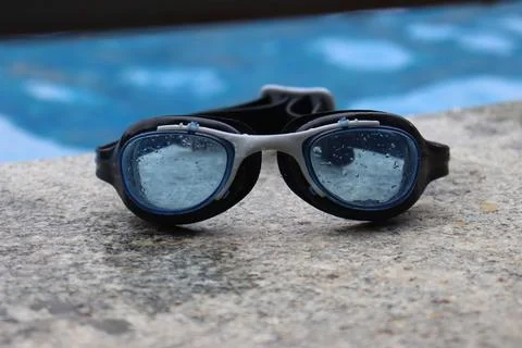 Swimming goggles placed by the side of a pool with blue pool on the background Stock Photos