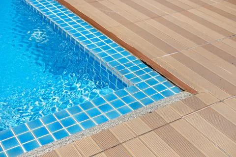 Swimming pool corner with clear blue water and tiled edge, featuring wooden Stock Photos