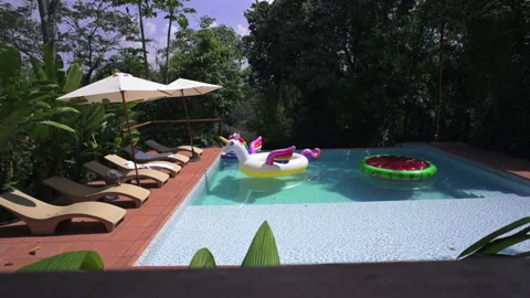 Swimming pool in rainforest lodge with inflatable unicorn float, Exotic Stock Footage 318511469