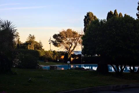 Swimming pool surrounded by trees in a park by the seaside at sunset Stock Photos