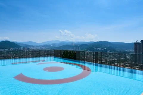 A swimming pool on top of a building overlooking some green mountainous lands Stock Photos