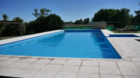 Swimming pool without people, blue, wind and sunny day, trees behind. Stock Footage 154309684