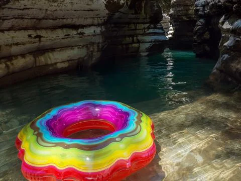 Swimming ring with a multicolored pattern on clear turquoise water in a shady Stock Photos