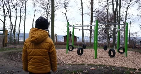 Swing in empty playground covered. A little boy looks at an empty playground Stock Footage 145225102