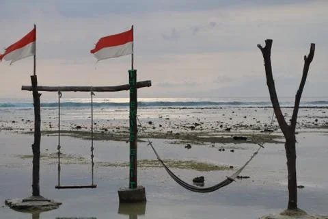 Swing, hammock and Indonesian flags during sunset on the ocean shore Foto stock