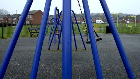 A swing in a kids playground moving back and forth on it's own. Stock Footage