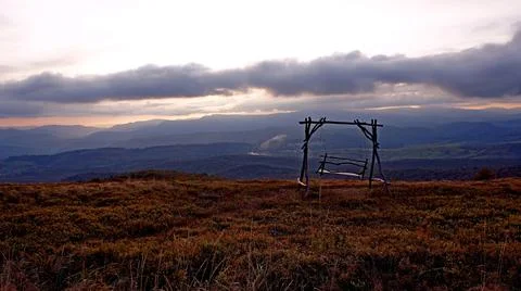 Swing somewhere high in the mountains on a background of clouds and sunset Stock Photos