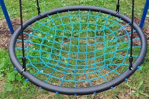 Swing is spider web with blue base against background of green grass. Stock-Fotos