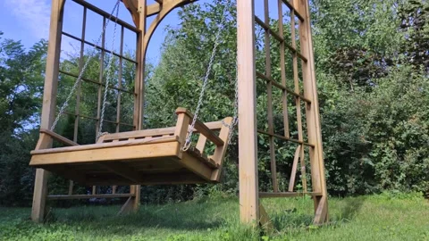 A swing without people sways against the backdrop of green trees. The concept of Stock Footage 136502951