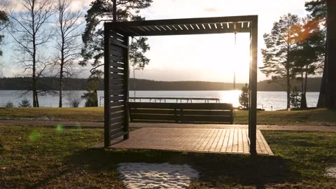 Swinging bench overlooking tranquil lake at sunset shine in coniferous park Stock Footage 299905523