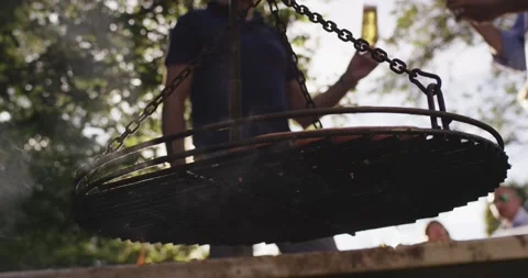 Swinging grill hanging on chains over a fire pit with the evening sun shining Vídeo Stock 339976759