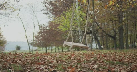 Swinging swing on empty public park in autumn. Leafs in playground on the floor 動画素材 140606922