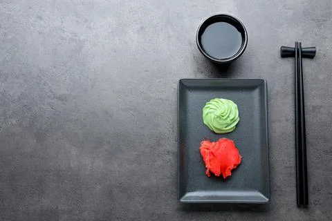 Swirl of wasabi paste, pickled ginger, soy sauce and chopsticks on grey table Stock Photos