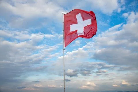 Swiss flag blowing in the wind, the background is a cloudy sky Stock Photos