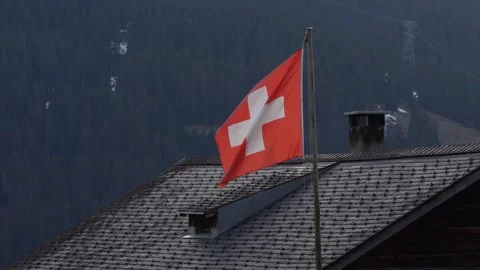 Swiss flag waving on a rooftop in the alps Vidéo 307013801
