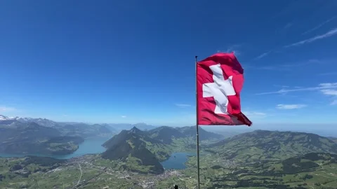 Swiss flag waving in the wind at the top of a mountain summit, overlooking a Stock Footage 345985002
