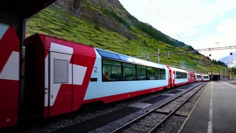 Swiss red Glacier Express train departing Zermatt, luxury alpine resort town Stock Footage 124548221