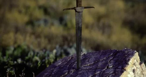 Sword embedded in rock at sunset amidst natural landscape Ilustración de archivo