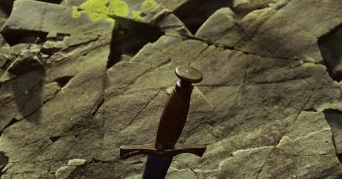 Sword embedded in rocky terrain with a rustic atmosphere at dusk Stock Illustration