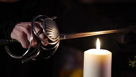 Sword glows over the flame of a wax candle 스톡 동영상 133077150