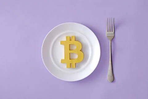 The symbol of the modern digital cryptocurrency Bitcoin in a plate and a fork Stock Photos