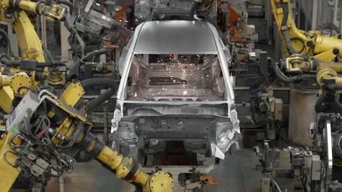 Symmetrical front view of multiple industrial robots working on a car chassis Stock Footage 332975875