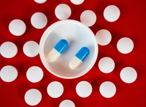 Symmetrical ring of round white tablets framing a lid with two blue capsules Stock Photos