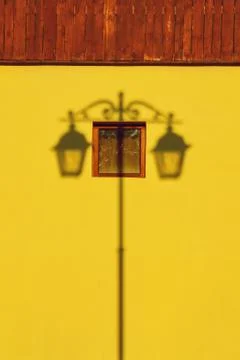 Symmetrical shadow from a street lamp on a yellow house with a small square w Stock Photos