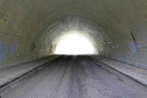 Symmetrical view of a bright light at the end of a dark concrete road tunne.. Stock Photos