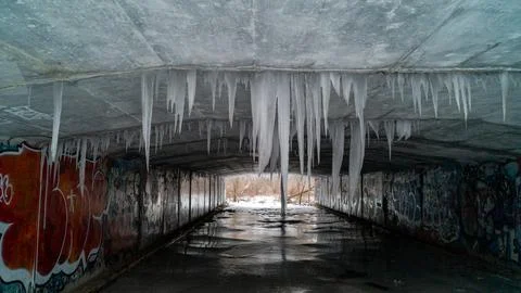 Symmetrical View of Massive Icicles Hanging Inside Concrete Graffiti Tunnel Stockfoto's