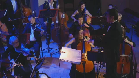 A symphony orchestra performs on stage with performers playing violins, cello Stock Footage