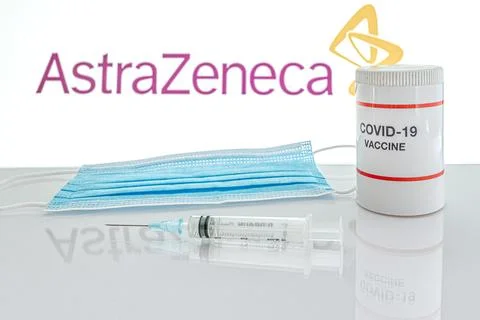 Syringe and facemask on a table in front of AstraZeneca logo Stock Photos