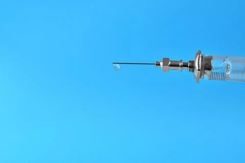 Syringe with a drop of medication at the end of the needle on a blue backgr.. Stock Photos