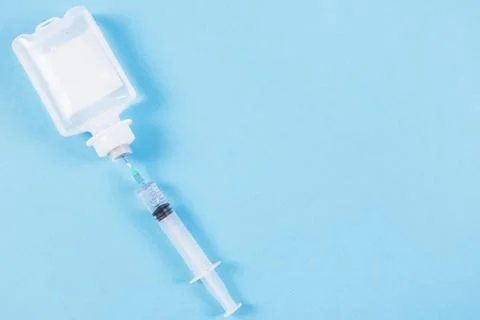 Syringe inserted normal saline solution plastic bottle blue background 库存照片