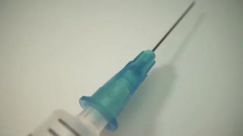 A syringe with a needle rotates on a white table. macro shot. Global coronavirus Stock Footage 143829116