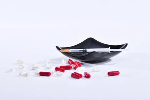 Syringe with needle surrounded by assorted pills Stock Photos