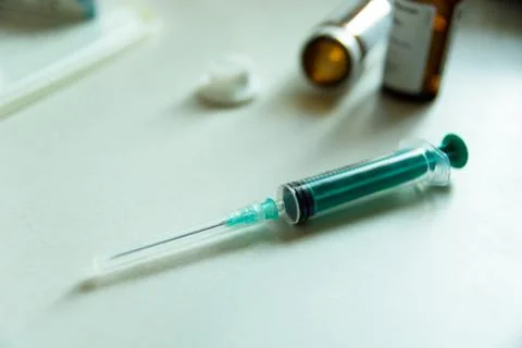 A syringe with a needle on the table top and a medicine pack Stock Photos