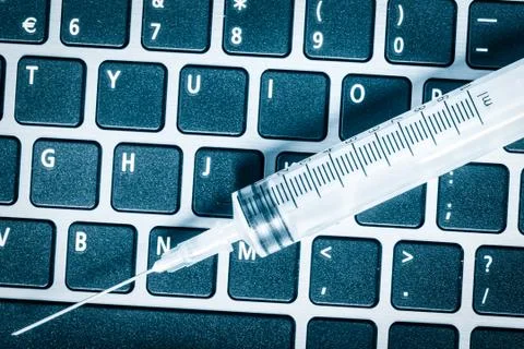 Syringe over a computer keyboard toned in blue Stock Photos