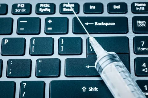 Syringe over a computer keyboard toned in blue Stock Photos