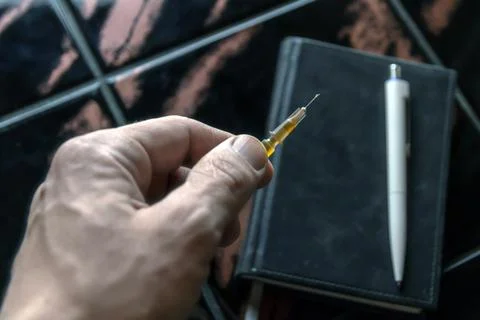 Syringe in a person's hand, on a notepad background, short focus, toning Stock Photos