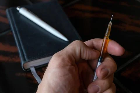 Syringe in a person's hand, on a notepad background, short focus, toning Stock Photos