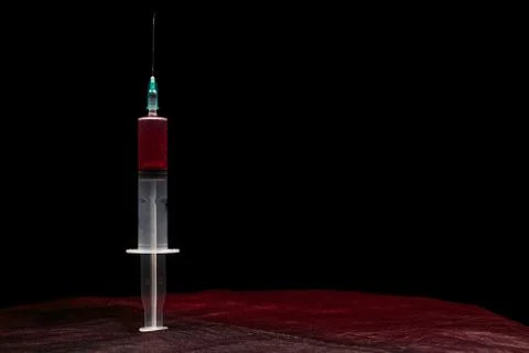 Syringe with red liquid on a red surface with dark copy space Foto stock