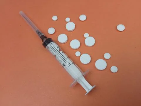 Syringe with white tablets on warm background Stock Photos