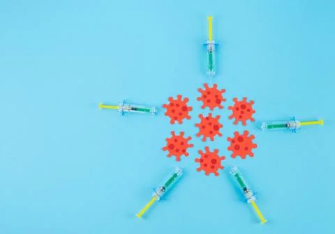 Syringes attacking red virus cluster on blue background. Copy space. Covid-19 Stock Photos